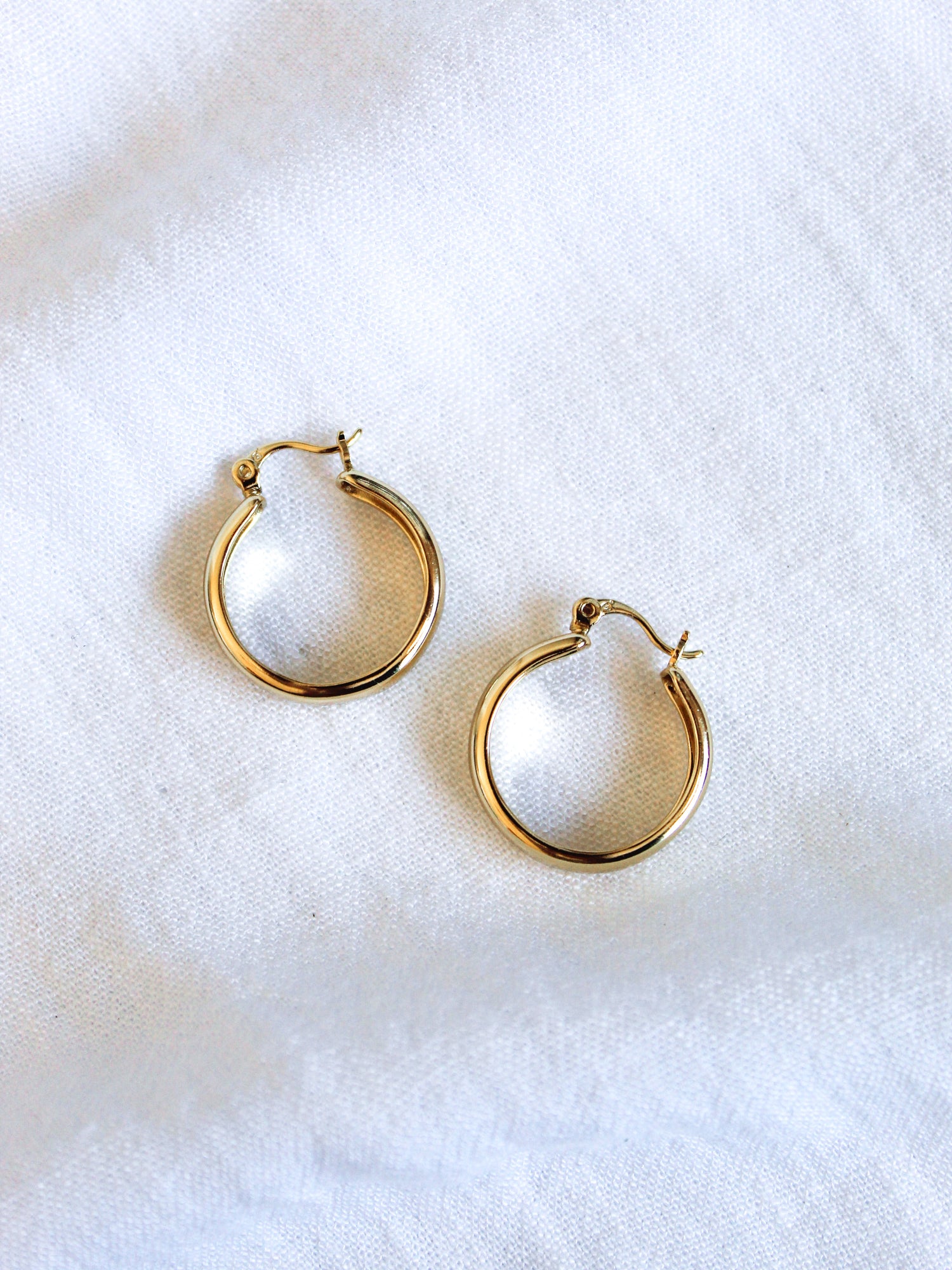 The Doreen earrings by Kinsey Designs Archives are small 14k gold filled hoops, .75 inch wide, displayed on a white fabric background.