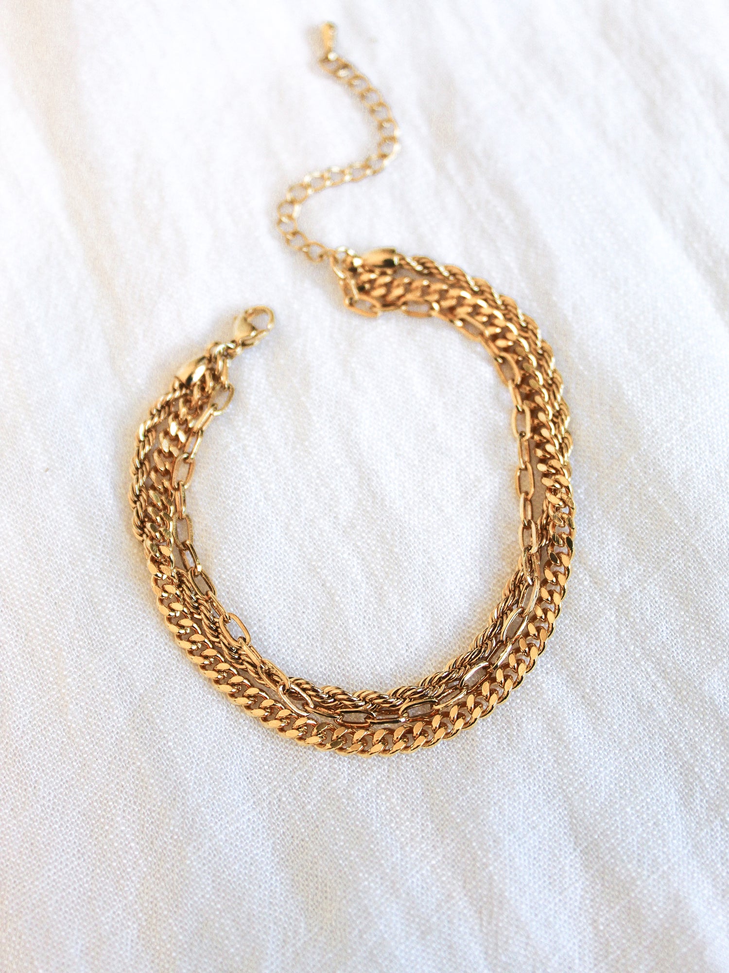 The Emmy Bracelet by Kinsey Designs Archives is a gold plated, multi-layered chain bracelet with a 6-inch length and optional extender, showcased on white textured fabric.