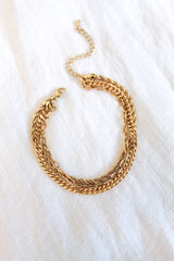 The Emmy Bracelet by Kinsey Designs Archives is a gold plated, multi-layered chain bracelet with a 6-inch length and optional extender, showcased on white textured fabric.