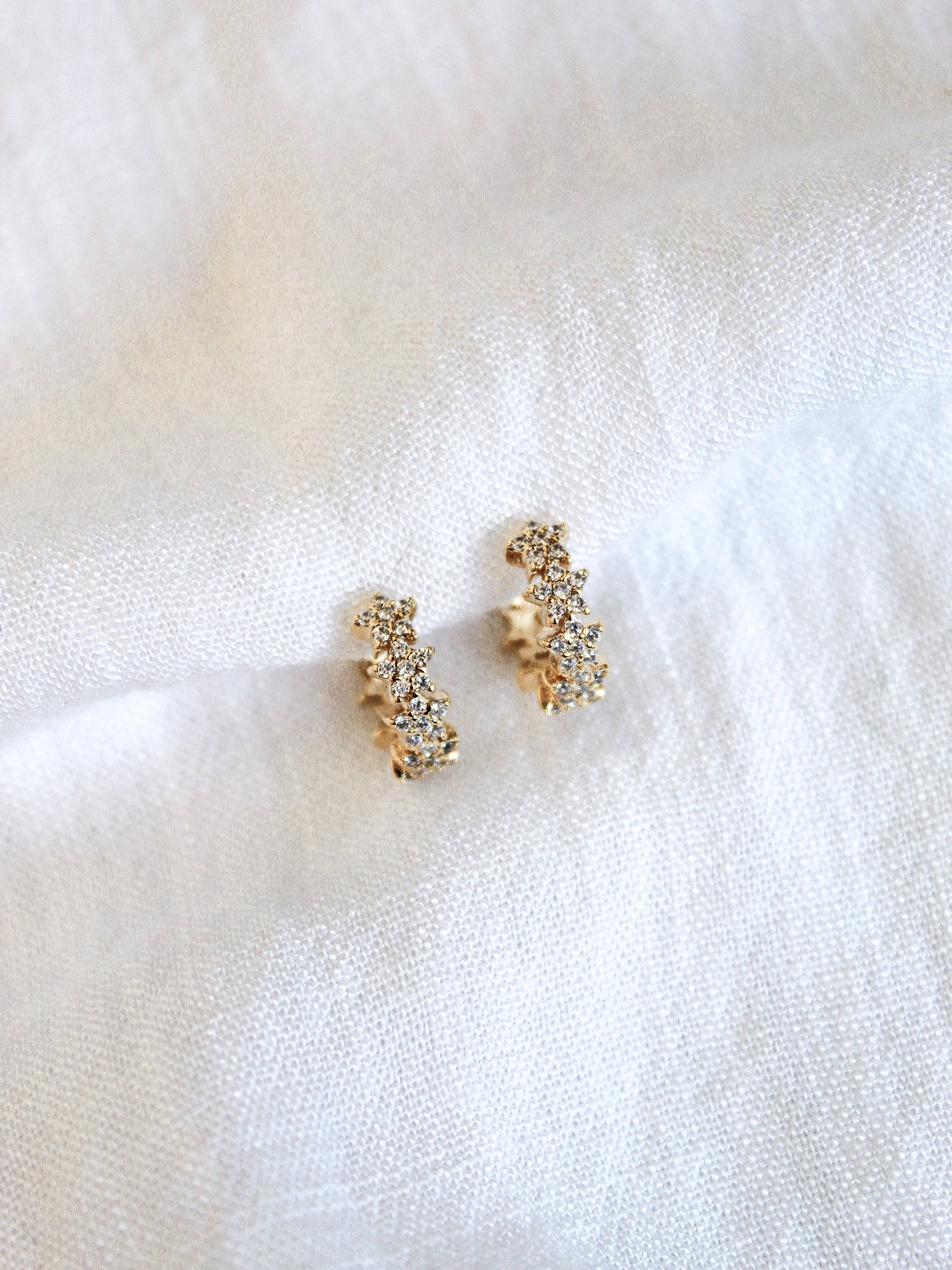 The Cloud Huggie by Kinsey Designs Archives shown on a soft, white textured fabric background, paired with a sparkling gold plated ring adorned with cubic zirconia.