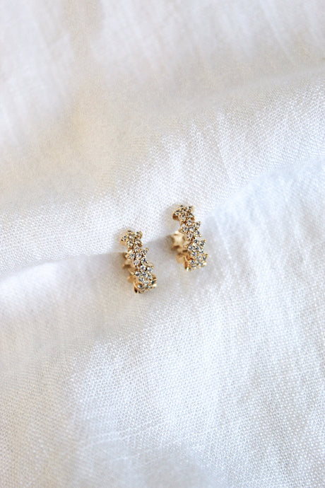 The Cloud Huggie by Kinsey Designs Archives shown on a soft, white textured fabric background, paired with a sparkling gold plated ring adorned with cubic zirconia.