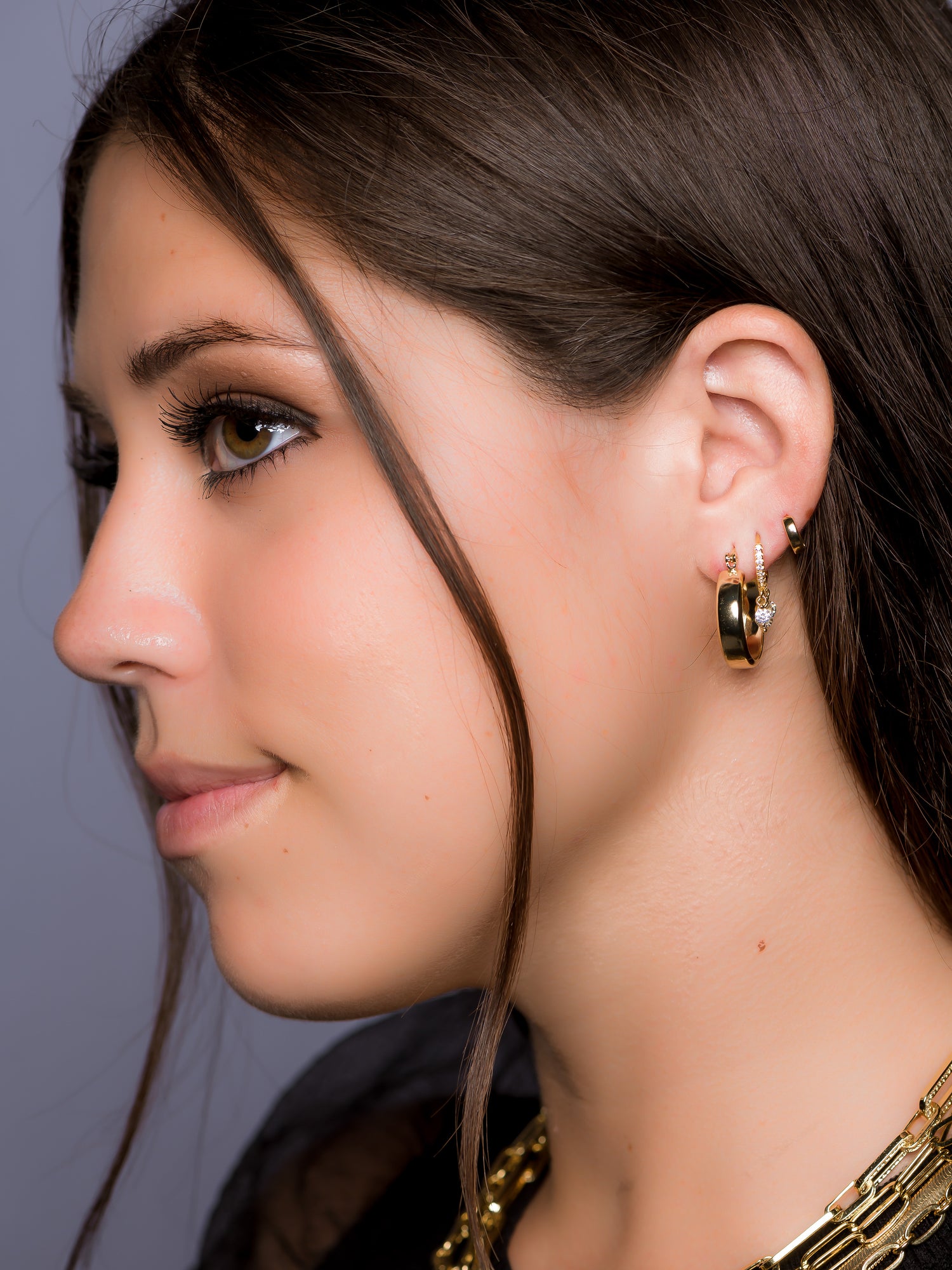 A woman in profile with long brown hair wears Kinsey Designs Archives’ Doreen gold filled necklace and gold hoop earrings, looking left.