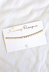 The Starry Choker by Kinsey Designs Archives, a gold-plated 14” necklace with a star charm, is displayed on a white branded card against white fabric for an elegant, stylish look.