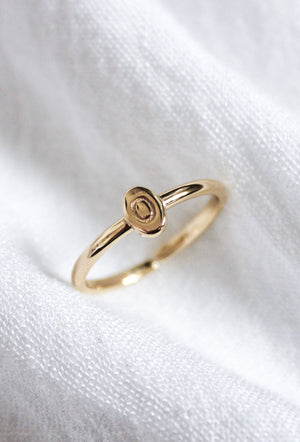 The Kinsey Initial Ring by Kinsey Designs features a small, oval-shaped design and rests on soft white textured fabric—a perfect piece of personalized jewelry.