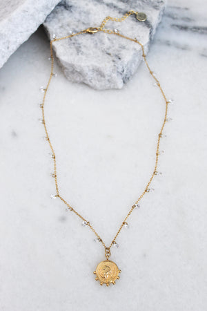 The Lover necklace by Kinsey Designs Archives features an 18k gold plated adjustable chain with a round pendant, small beads, and CZ charms. Shown on marble with stone accents, it adds elegance to any look.