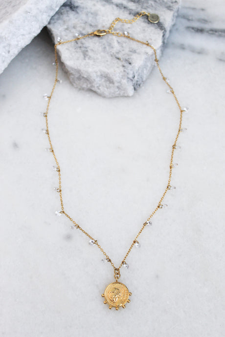 The Lover necklace by Kinsey Designs Archives features an 18k gold plated adjustable chain with a round pendant, small beads, and CZ charms. Shown on marble with stone accents, it adds elegance to any look.
