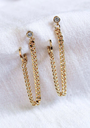 The Kinsey Designs Knox Double Earring features gold-plated hoops with chain links and small round cubic zirconia at the posts, ideal for double piercings, shown on white fabric.