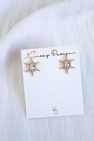 The Faye Stud gold star-shaped earrings by Kinsey Designs feature sparkling cubic zirconia on a branded card, displayed against light fabric. Add shine to your style—shop the sample sale now!.