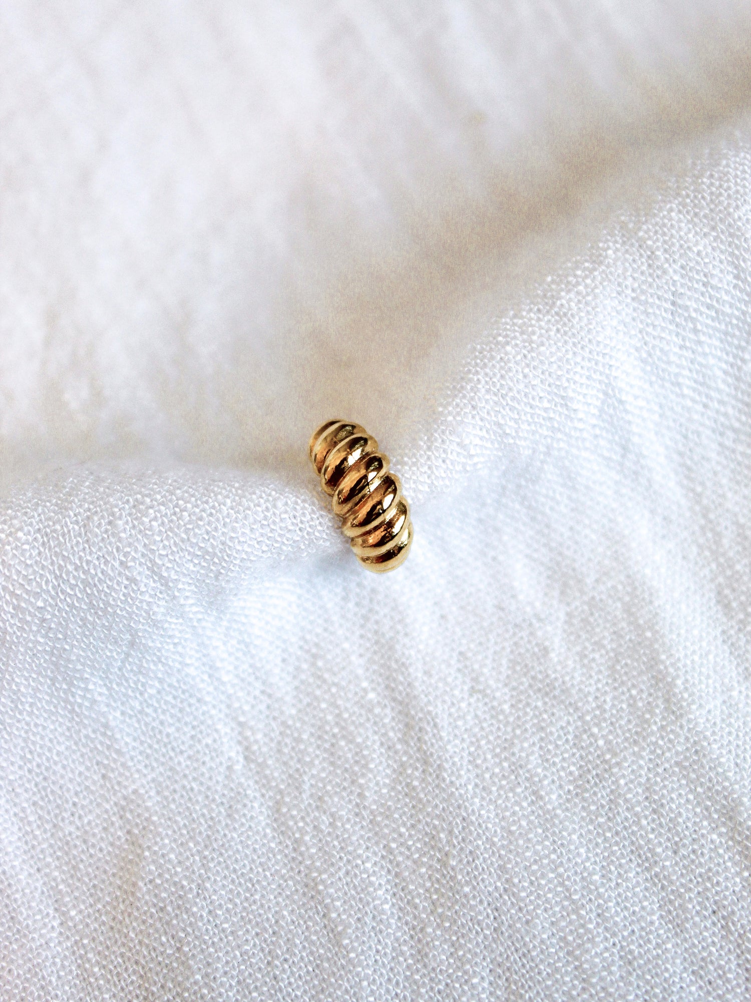 The Metz Cuff by Kinsey Designs Archives, a small gold-plated ridged piece, rests on soft white textured fabric.