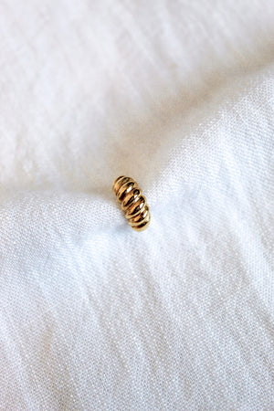 The Metz Cuff by Kinsey Designs Archives, a small gold-plated ridged piece, rests on soft white textured fabric.