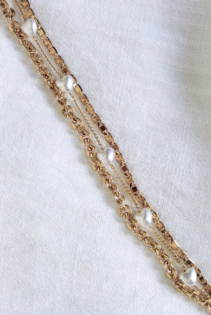 The Beyah Layer Bracelet by Kinsey Designs Archives features gold-plated brass chains with small pearls, displayed diagonally on a white textured fabric background.