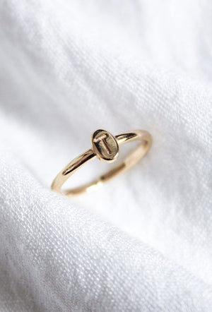 The Kinsey Initial Ring by Kinsey Designs features an engraved letter "T" and is displayed on soft white fabric—a timeless, personalized jewelry piece.