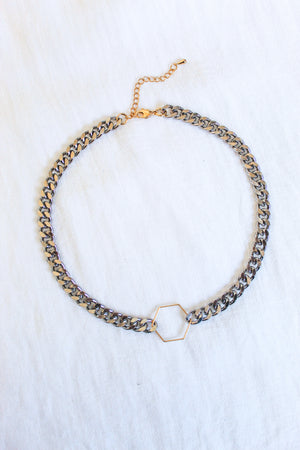 The Fraser Necklace by Kinsey Designs Archives features a 17-inch silver chain with a gold hexagon pendant, crafted from rhodium-plated brass and finished with an adjustable clasp and extender, displayed on white fabric.