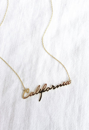 The State of Mind Necklace by Kinsey Designs Archives features a "California" nameplate and is shown on a white textured fabric background.