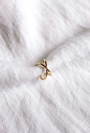 The Criss-Cross Ear Cuff from Kinsey Designs Archives, gold plated with a .5" circumference, rests on soft, white textured fabric.
