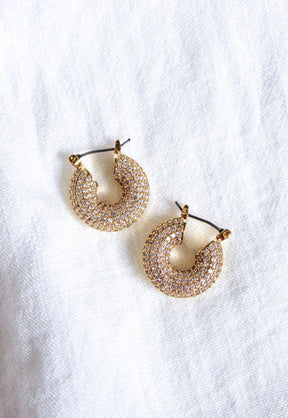 The Mikki Pave Hoop by Kinsey Designs Archives features gold plating and sparkling stones, measuring .75" wide, showcased on a white textured fabric background.