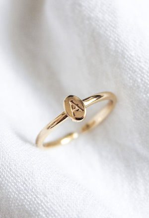 The Kinsey Initial Ring Letter A from the Kinsey Designs Collection features an engraved "A" on an oval gold face, showcased on white textured fabric.