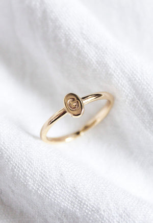 The Kinsey Designs Collection Kinsey Initial Ring Letter G features a gold band with a small oval top engraved with the letter "G," shown on white fabric.