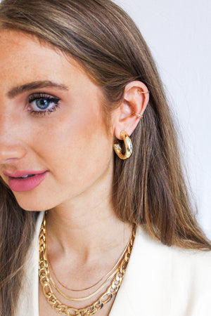 Woman with long brown hair wears Kinsey Designs' Jasmine Hoops, layered gold-filled necklaces, and a cream blazer for a standout jewelry look.