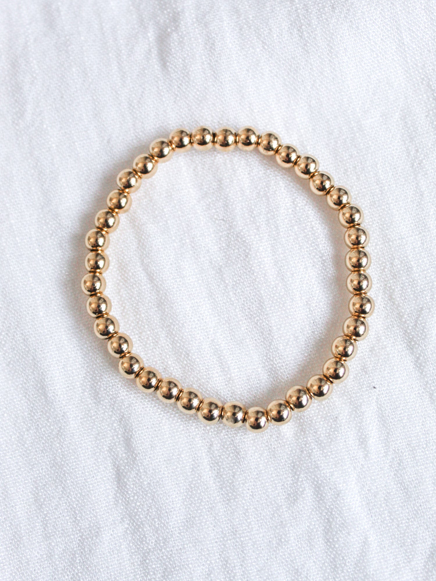 The Liam Stacking Bracelet by Kinsey Designs, shown in a circle on white fabric, features an adjustable stretch design and is available in multiple sizes.