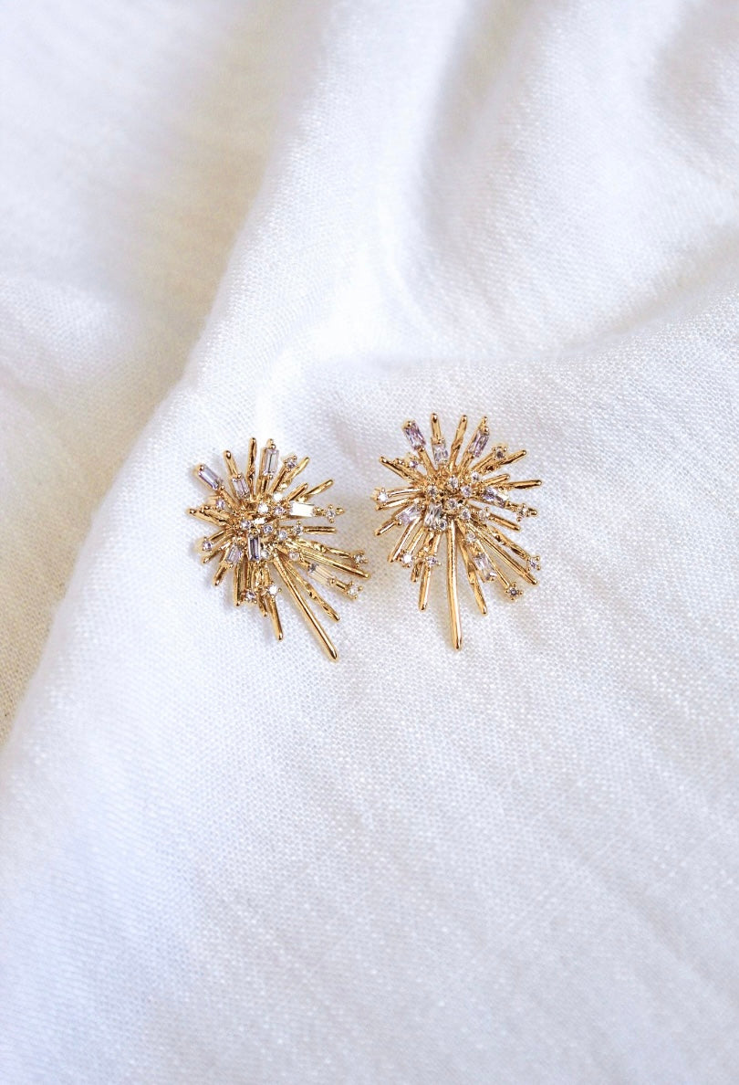 The Harlem Post earrings by Kinsey Designs Archives feature gold plating and cubic zirconia accents, displayed on textured white fabric. At 1” long, they offer a subtle, radiant touch.