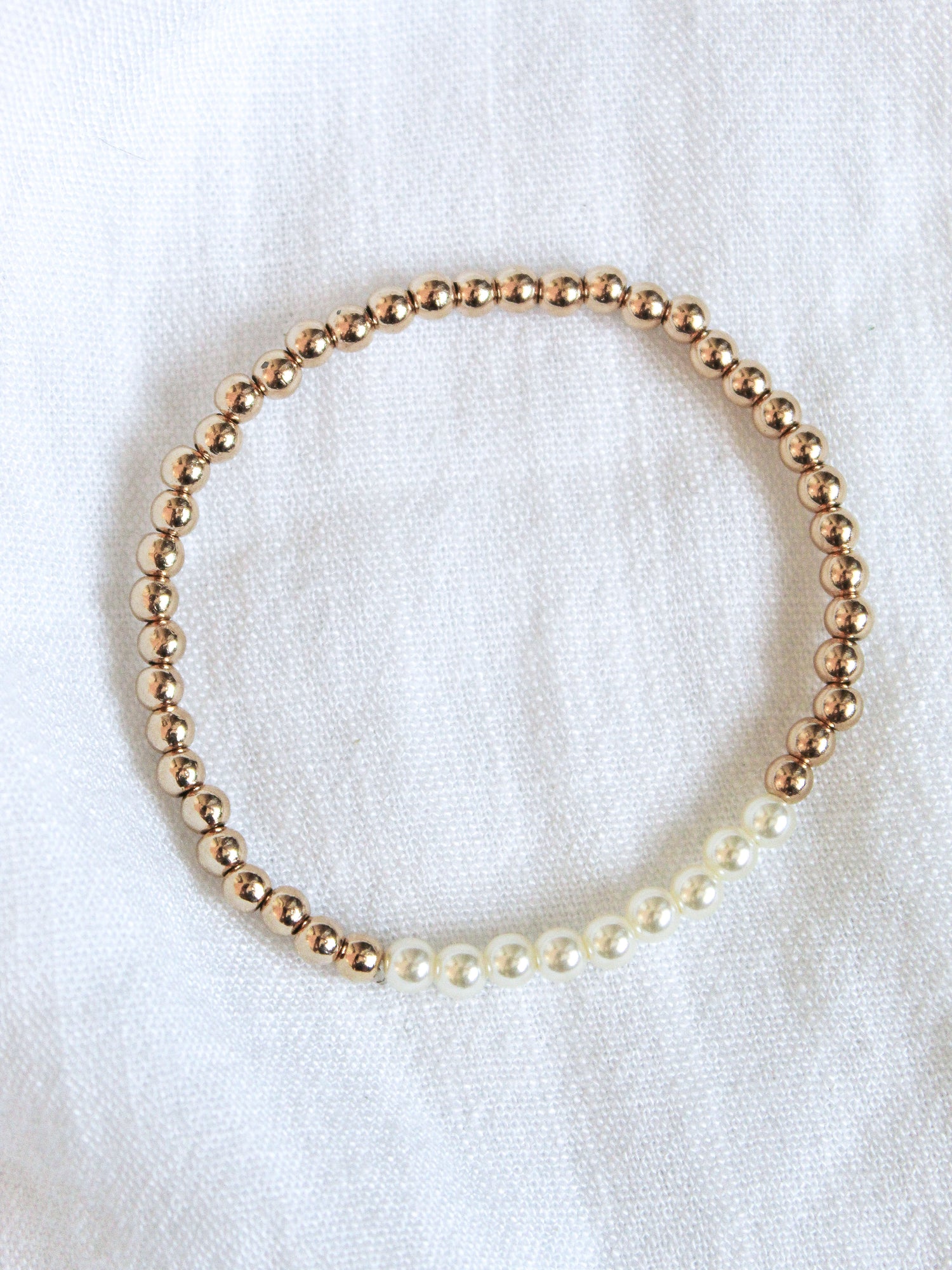 The Kinsey Designs Liam Stacking Bracelet features gold filled and white pearls on a white fabric background, with an adjustable stretch for a comfortable fit. Available in multiple sizes.