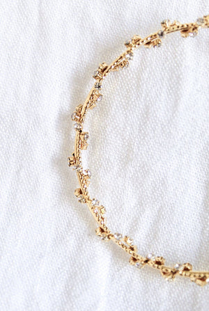 The Staci Hoop by Kinsey Designs Archives, featuring gold plating and delicate cubic zirconia crystals, is displayed on a soft white textured fabric background.