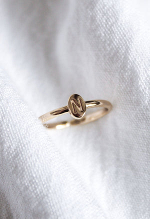The Kinsey Initial Ring Letter N from the Kinsey Designs Collection features a gold ring with a round plate engraved with the letter "N," shown resting on white fabric.