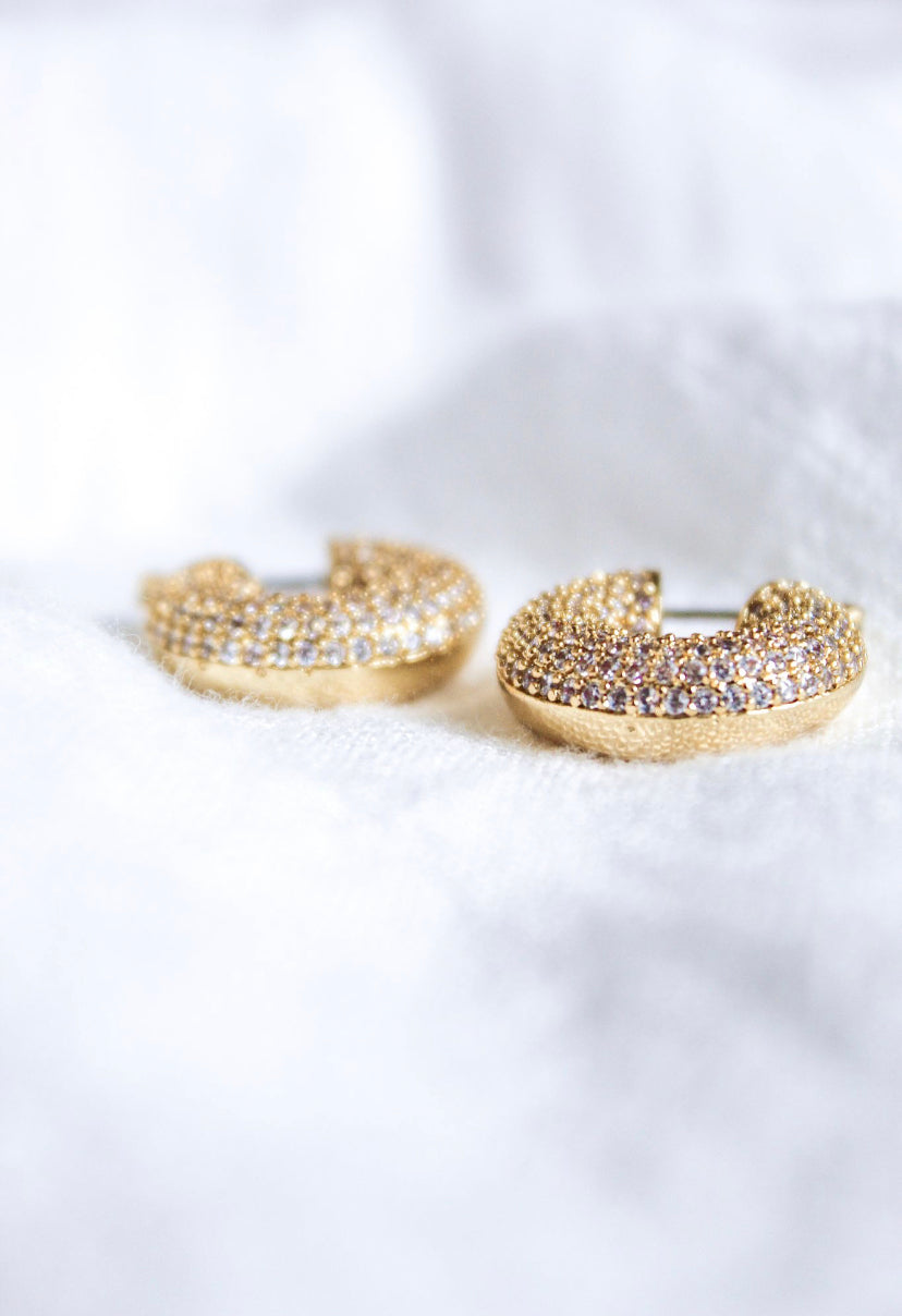 The Mikki Pave Hoop earrings by Kinsey Designs Archives, featuring gold plating and small sparkling stones, each .75" wide, are displayed on a soft white fabric background.