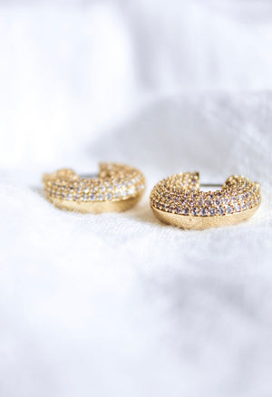 The Mikki Pave Hoop earrings by Kinsey Designs Archives, featuring gold plating and small sparkling stones, each .75" wide, are displayed on a soft white fabric background.