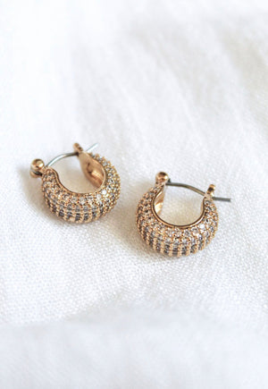 The Stevie 2-Way Hoop by Kinsey Designs Archives features gold-plated huggie hoops with small clear cubic zirconia crystals, shown on a white fabric background.
