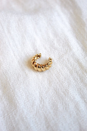 The Metz Cuff by Kinsey Designs Archives, a gold-plated textured ear cuff, rests on a soft white fabric surface.