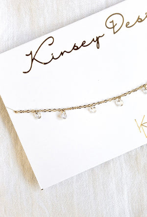 The Clare Choker by Kinsey Designs Archives features a gold plated 14-inch chain with small clear cubic zirconia pendants, displayed on a branded card.