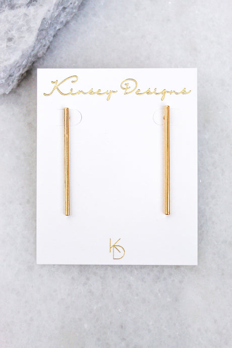 Walker gold bar earrings by Kinsey Designs Archives, featuring a surgical steel post, shown on a white branded card against a light marble background.