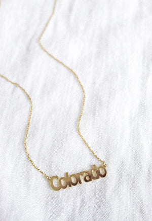 The Kinsey Designs Archives State of Mind Necklace features a "Colorado" pendant, shown on white fabric. Celebrate your hometown pride with this timeless piece from our State of Mind collection.