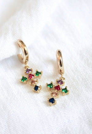 The Tori Huggie - Clear by Kinsey Designs Archives features gold filled hoops with dangling clear cubic zirconia crosses, displayed on a white fabric background.